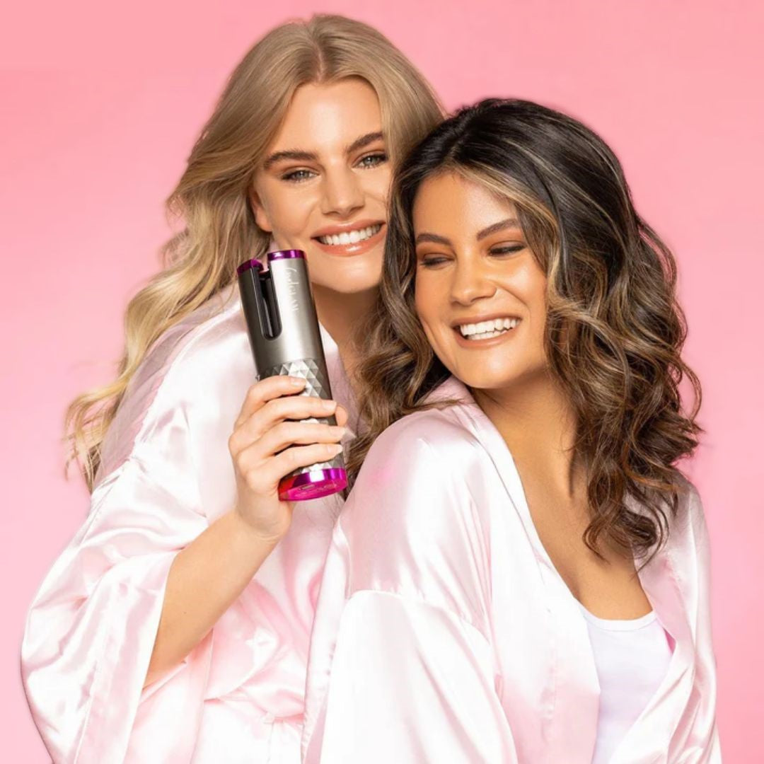 Zwei Frauen in rosa Bademänteln mit automatischem Lockenstab auf rosa Hintergrund.