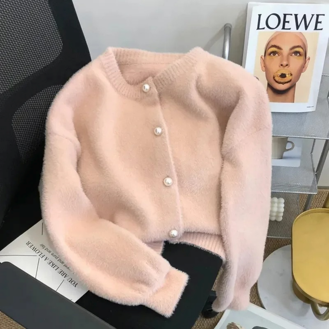 Rosa Strickjacke mit Rundhalsausschnitt und Perlenknöpfen auf Stuhl, modisch, elegant.
