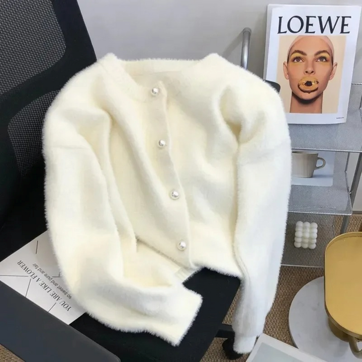 Weißer Strick-Cardigan mit Rundhalsausschnitt und Knöpfen auf schwarzem Stuhl.