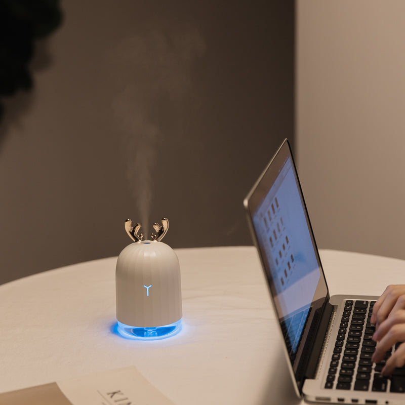 Weißer Luftbefeuchter mit Rentiergeweih-Design und blauer LED-Beleuchtung auf Tisch.