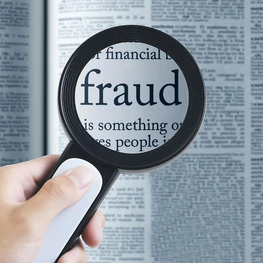 Vergrößerungsglas über Zeitungstext mit Fokus auf "Fraud", Hand hält Lupe, Betrug, Finanzthemen.