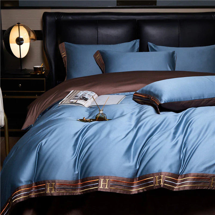 Luxuriöses blaues Bettwäsche-Set aus Seide mit braunen Akzenten und Kissen auf einem Bett.