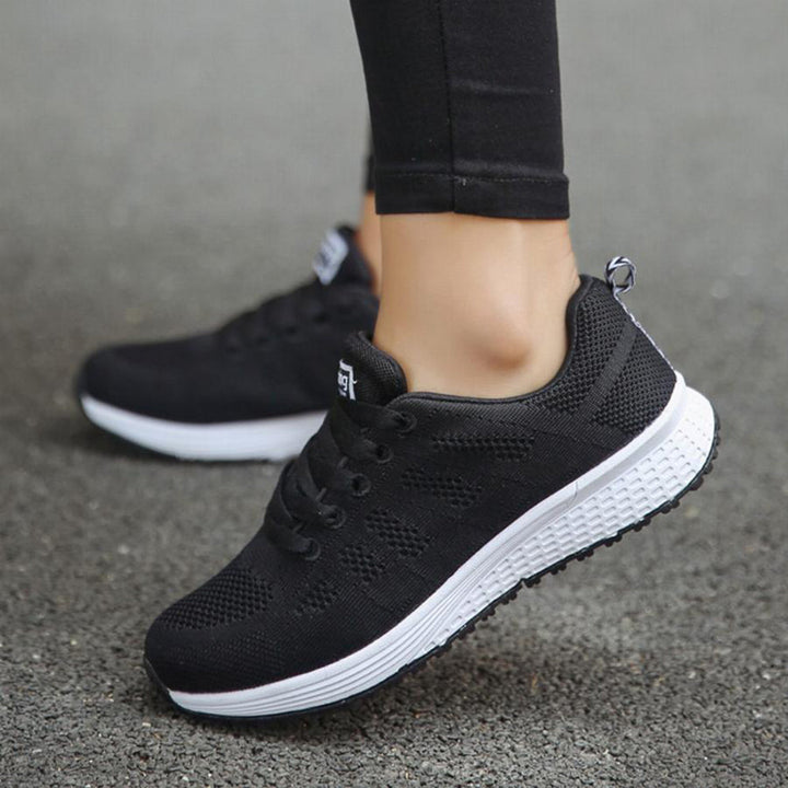 Schwarze Damen-Laufschuhe, atmungsaktiv, rutschfest, mit weißer Sohle auf Asphalt.
