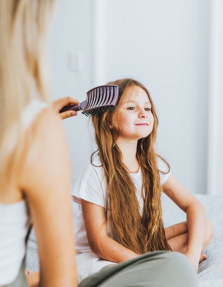 Mädchen mit langen Haaren wird mit lila Kamm gekämmt, Kind, Haarpflege, Zuhause.