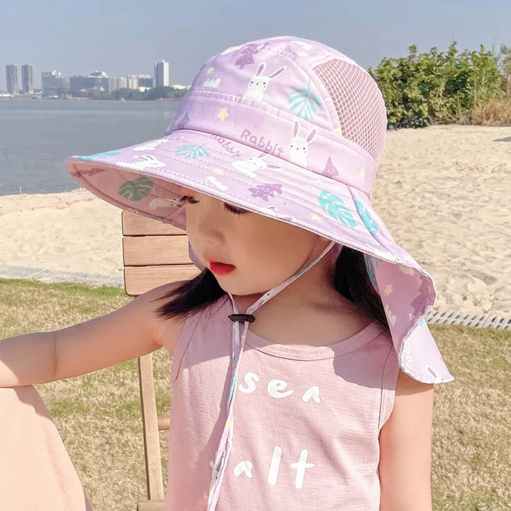 Mädchen mit lila Sonnenhut am Strand, Sommermode, Kindermode, UV-Schutz, Freizeitkleidung.
