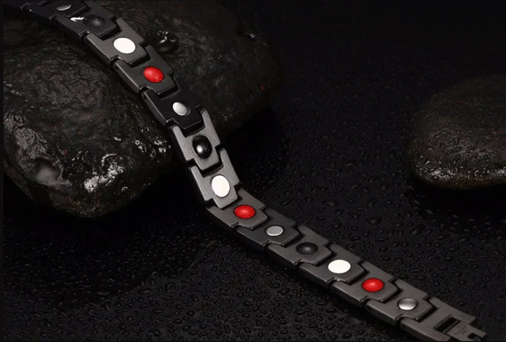 Schwarzes magnetisches Armband mit roten und weißen Elementen auf nassem Stein.