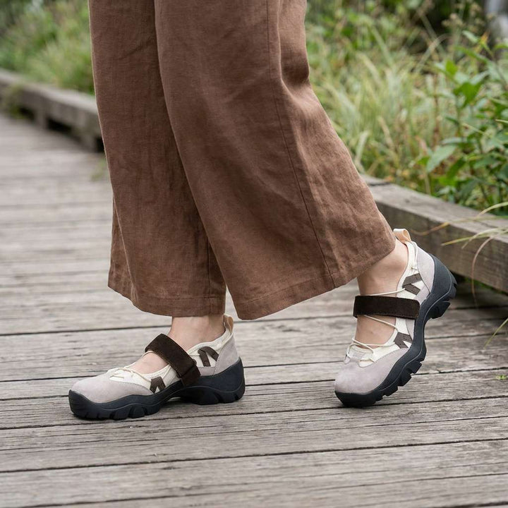 Béžové mokasíny s hnědým páskem na suchý zip, na nohou modelky v hnědých lněných kalhotách na dřevěné lávce. 11
