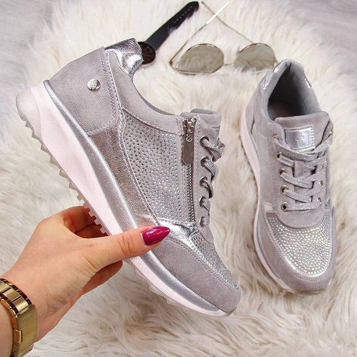 Silberne Damen-Sneaker mit Glitzer, Reißverschluss und Schnürsenkeln auf weißem Fellteppich.