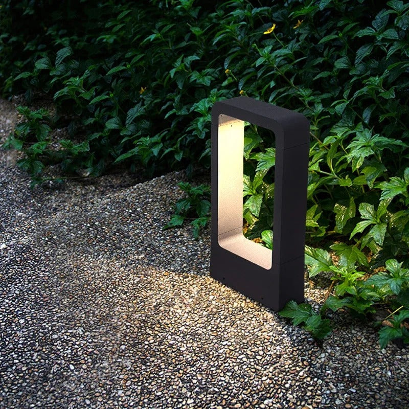 Moderne schwarze LED-Gartenleuchte, rechteckig, beleuchtet Weg neben grünem Laub.