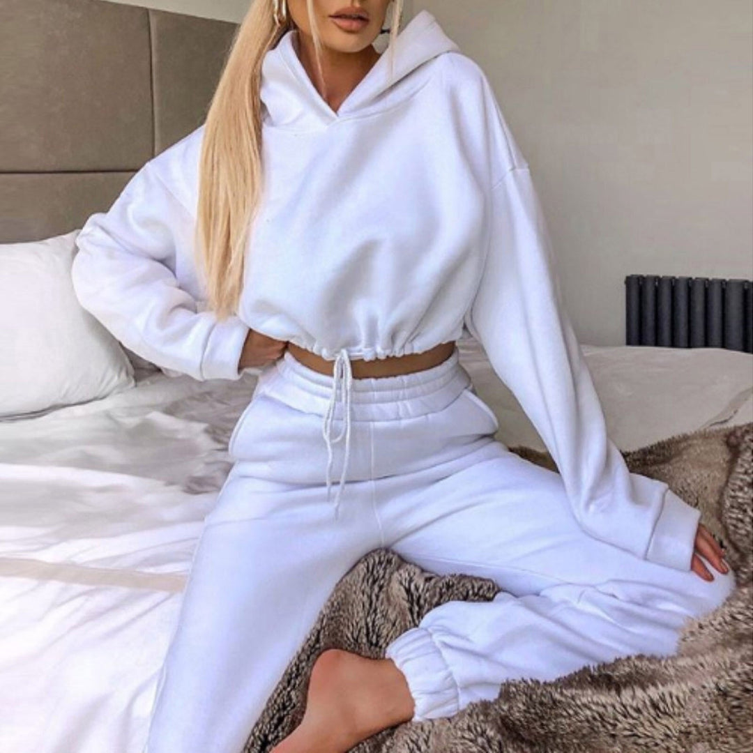 Frau in weißem Hoodie und Jogginghose auf Bett, gemütliche Damenmode, Freizeitkleidung.