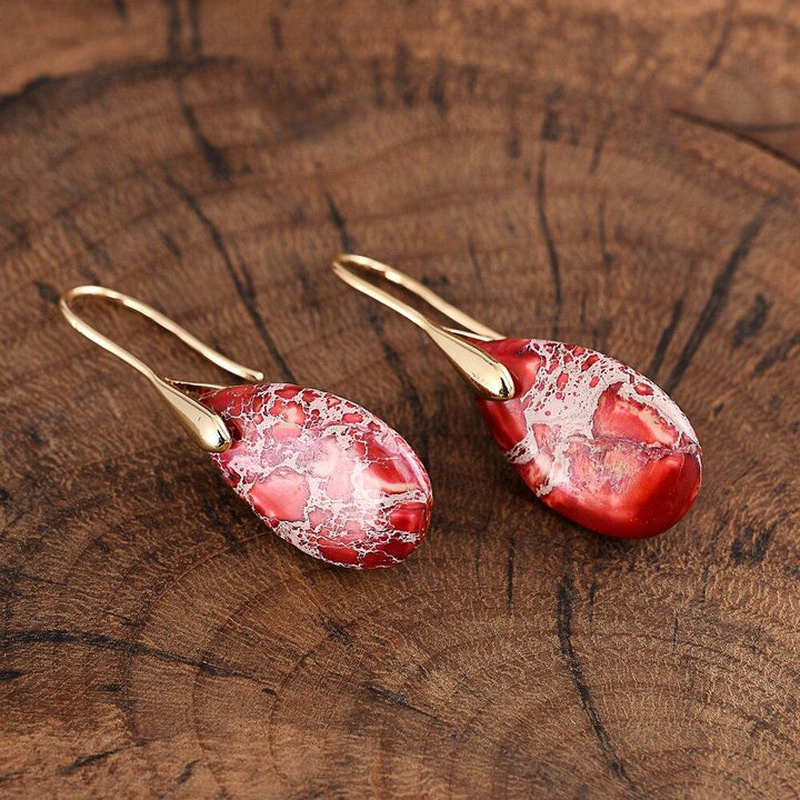 Rote Regalit Ohrringe, Tropfenform, goldene Haken, handgefertigter Schmuck, Holzuntergrund.