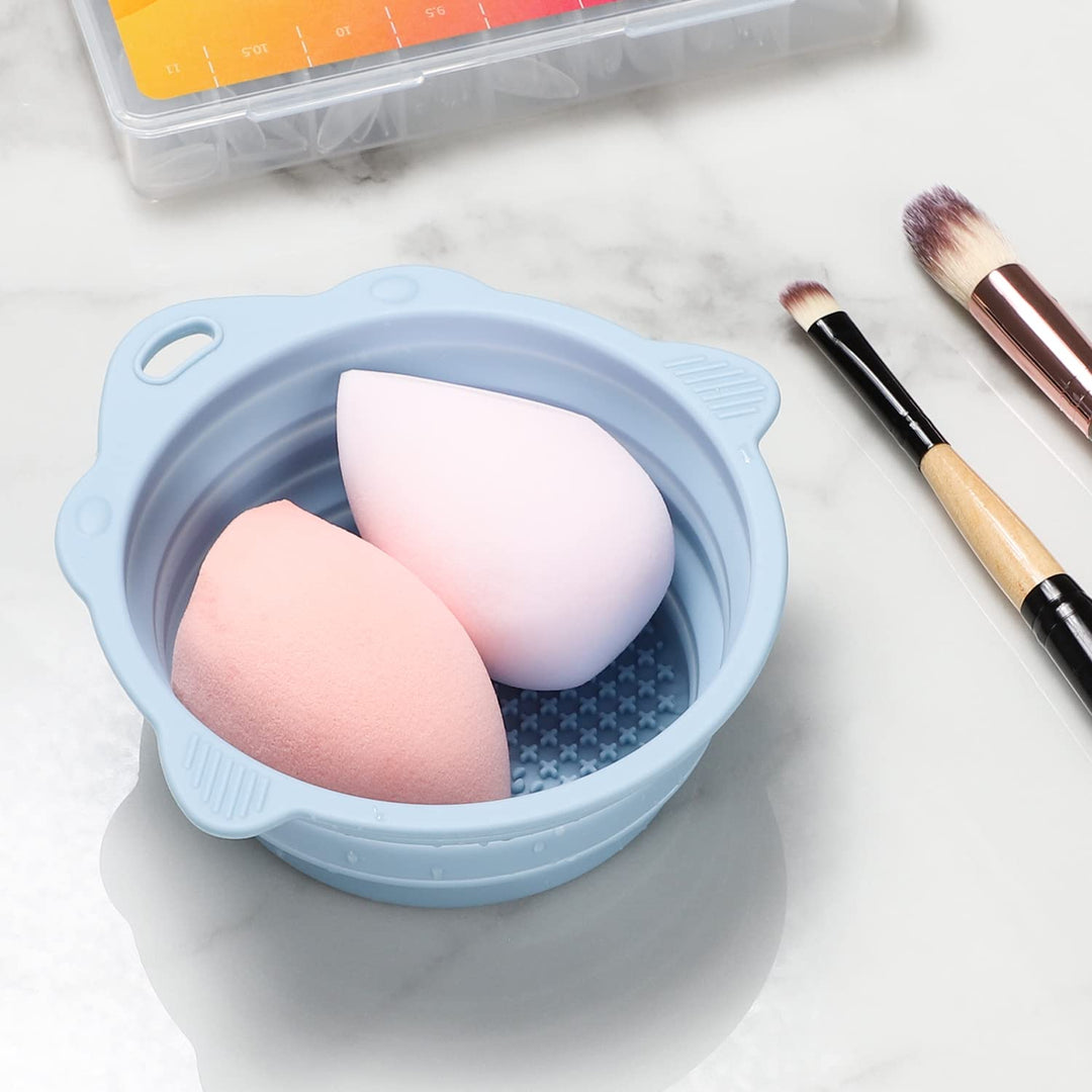 Zwei Make-up-Schwämme in blauem Silikon-Reinigungsbehälter auf Marmoroberfläche, mit Pinseln.