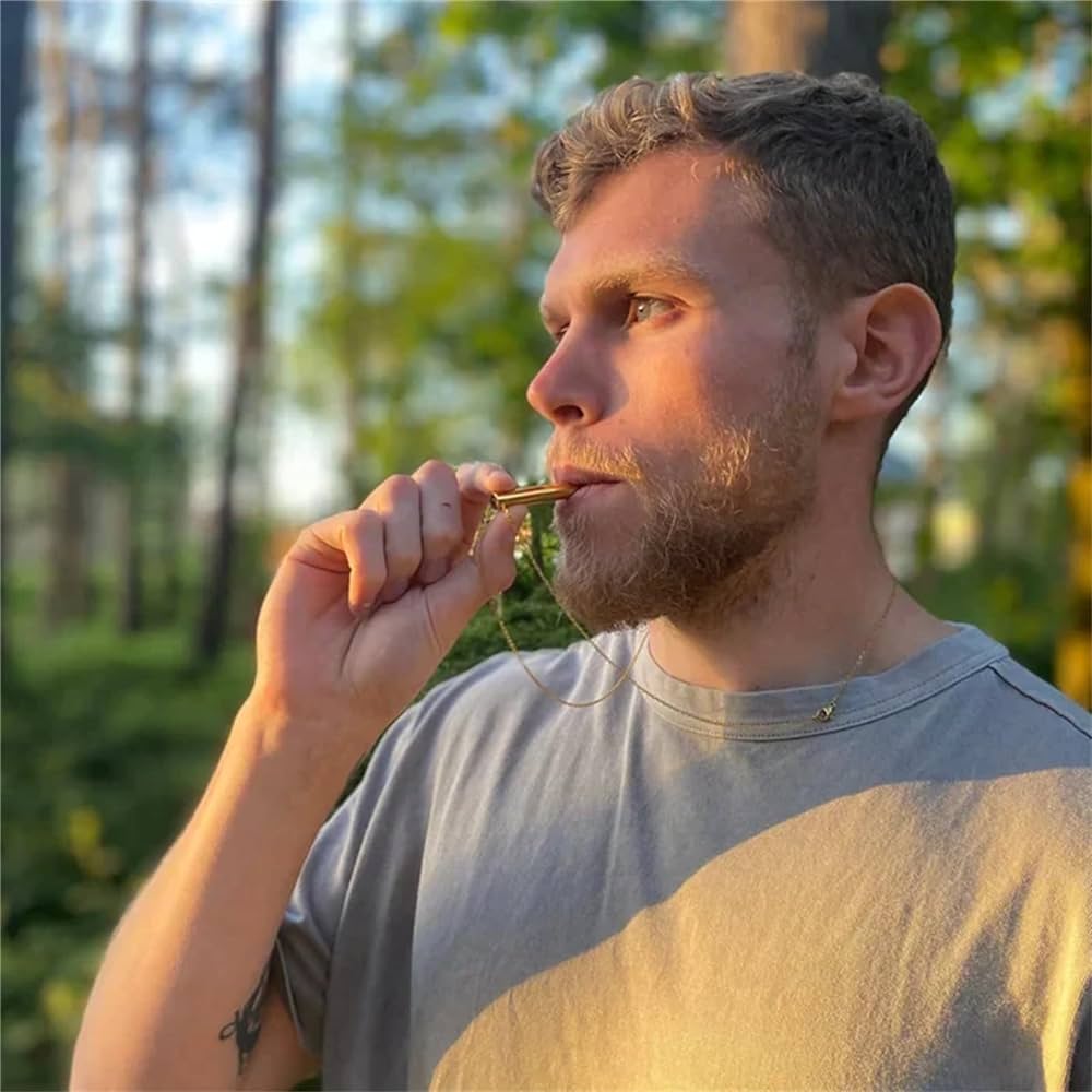 Mann mit Bart im Wald, bläst in goldene Notfallpfeife, Outdoor-Survival-Ausrüstung.