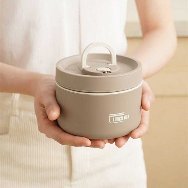 Beigefarbene, tragbare, isolierte Lunchbox aus Kunststoff, rund, mit Griff, in Händen gehalten.