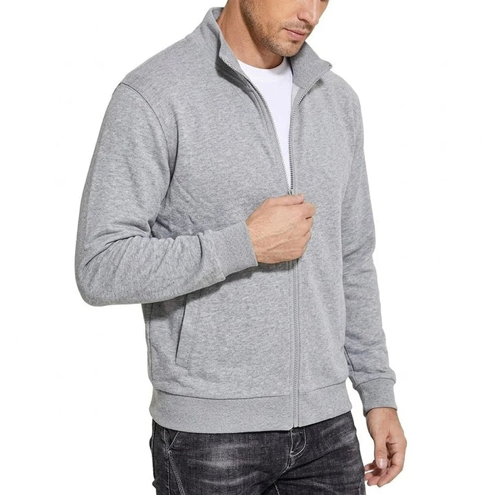 Světle šedá mikina na zip se stojáčkem na modelovi, snímek z polobočního pohledu, ruka drží zip a vidět je žebrovaný lem. 2
