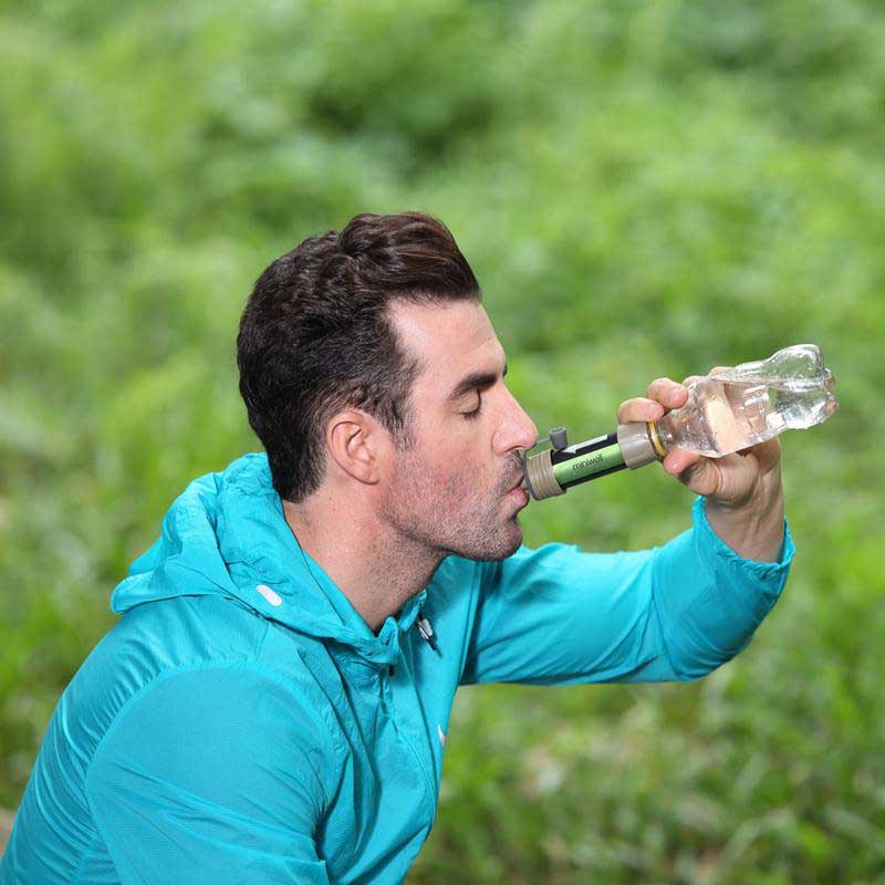 Mann trinkt aus tragbarem Wasserfilter in grüner Natur, Miniwell Wasserfilter, Outdoor-Aktivität.