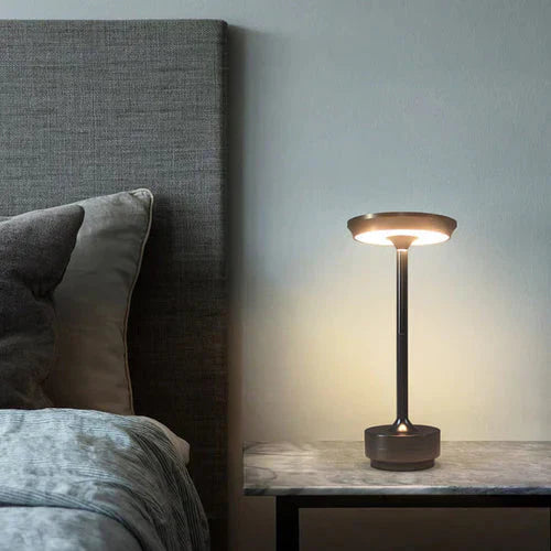 Moderne Nachttischlampe aus Metall, LED, dimmbar, auf Marmortisch neben grauem Bett.