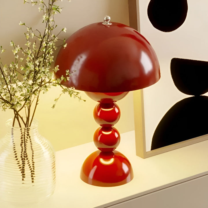 Rote, kugelförmige Tischlampe, modern, dekorativ, aus Metall, neben Vase mit Zweigen.