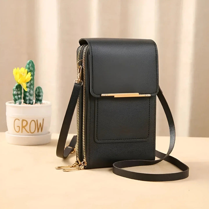 Schwarze Leder-Handytasche mit Reißverschluss und Schulterriemen, neben kleinem Kaktus.
