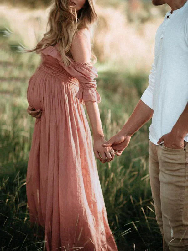 Schwangere Frau im rosa Kleid hält Hand eines Mannes, romantische Outdoor-Szene.