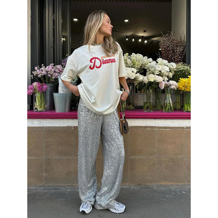 Frau in silberner Paillettenhose und weißem T-Shirt vor Blumenladen.