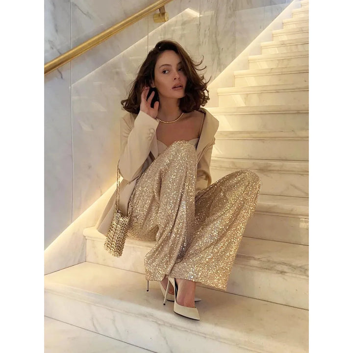 Frau in goldener Paillettenhose auf Marmortreppe, elegantes Outfit, Abendmode, glamourös.