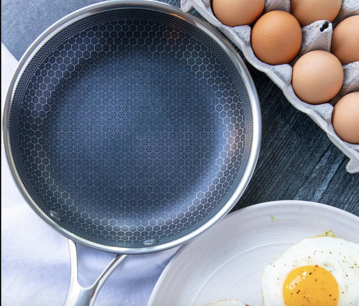 Bratpfanne aus Edelstahl mit Antihaftbeschichtung, neben Eiern und Spiegelei auf Holztisch.