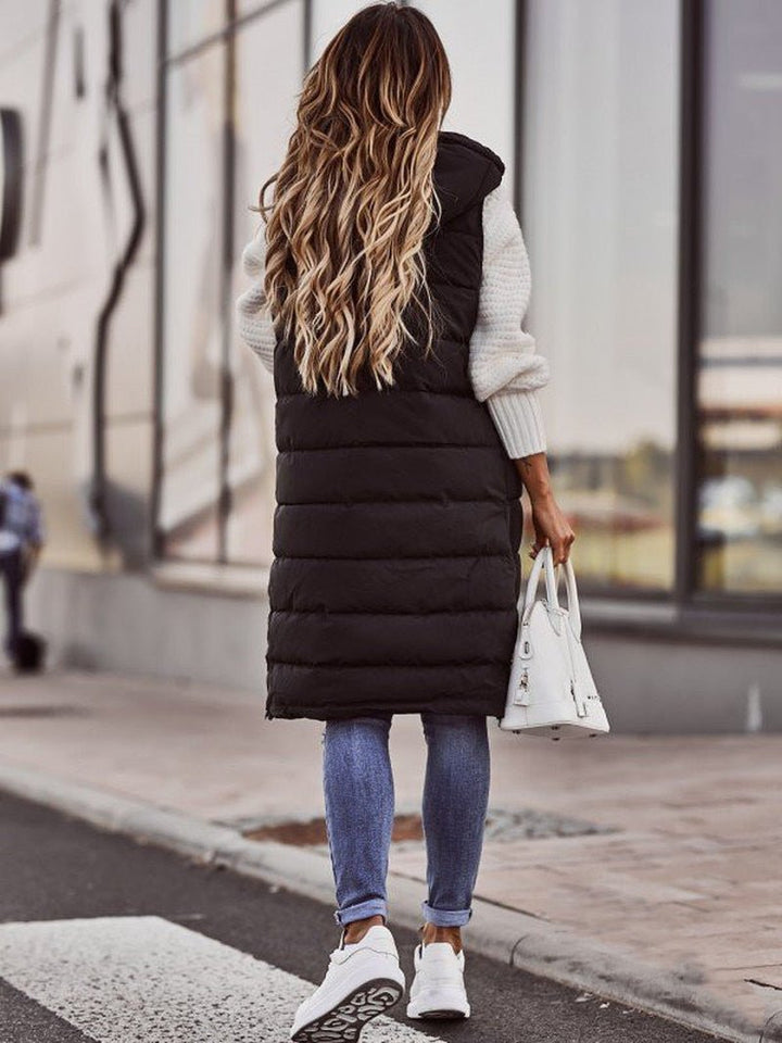 Frau in schwarzer, knielanger Steppweste, blaue Jeans, weiße Sneakers, weiße Handtasche.