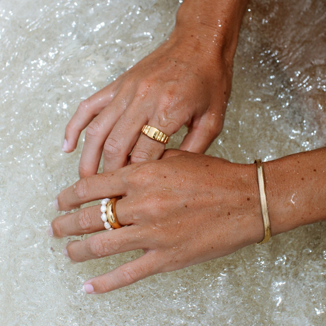 Hände mit goldenen Ringen und Armband im Wasser, Perlenring, Schmuck, Modeaccessoires.