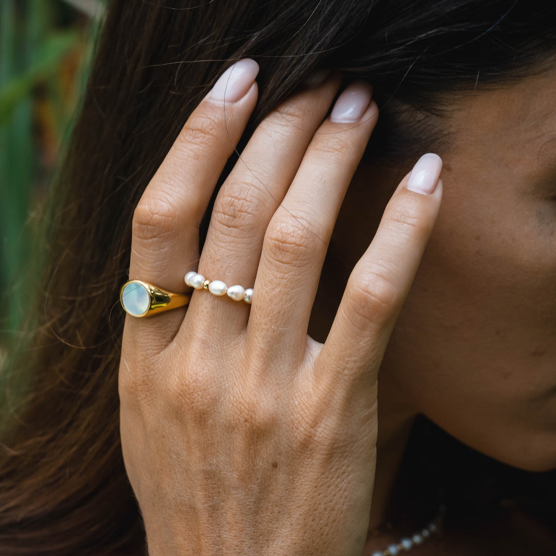 Frau mit Perlenring und goldfarbenem Siegelring, Nahaufnahme, eleganter Schmuck, Hand.