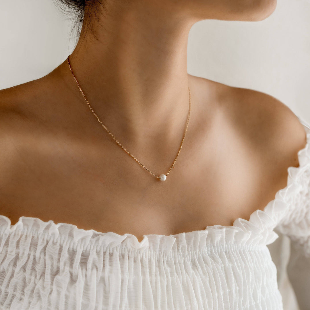 Frau trägt goldene Halskette mit Perle, eleganter Schmuck, minimalistisches Design.