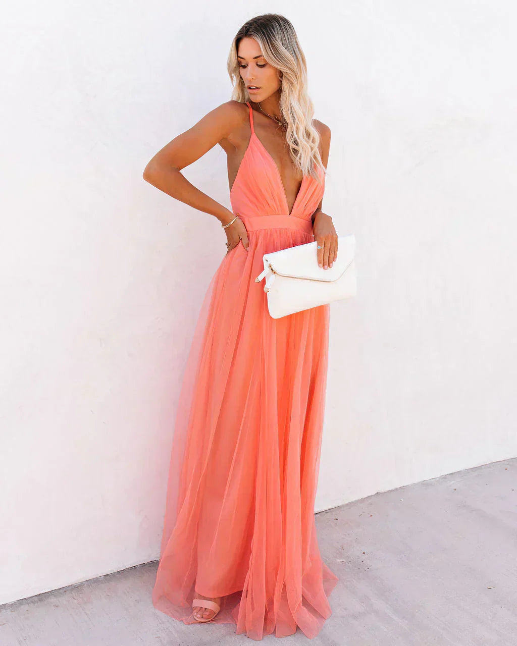 Frau in apricotfarbenem Maxikleid aus Tüll, elegantes Abendkleid, Sommermode, weiße Clutch.