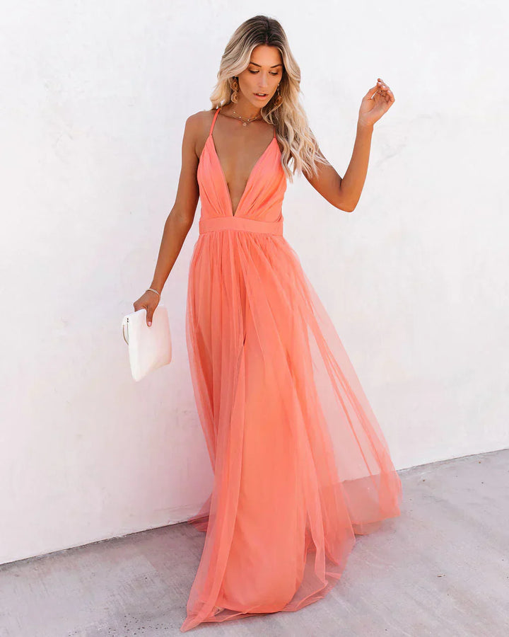 Frau in apricotfarbenem Maxikleid aus Tüll, tiefem Ausschnitt, hält weiße Clutch, elegante Mode.