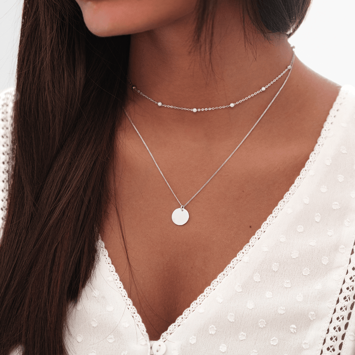 Frau mit silberner Halskette, rundem Anhänger, elegantes Schmuckdesign, modisches Accessoire.