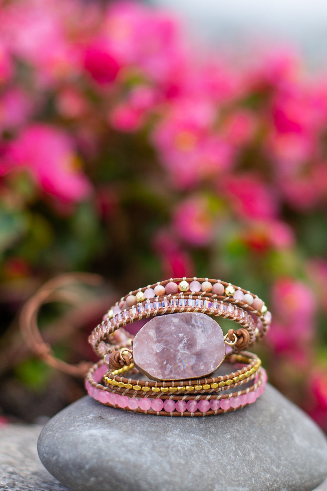Rosa Edelstein-Armband auf Stein, umgeben von rosa Blumen, handgefertigter Schmuck, Boho-Stil.