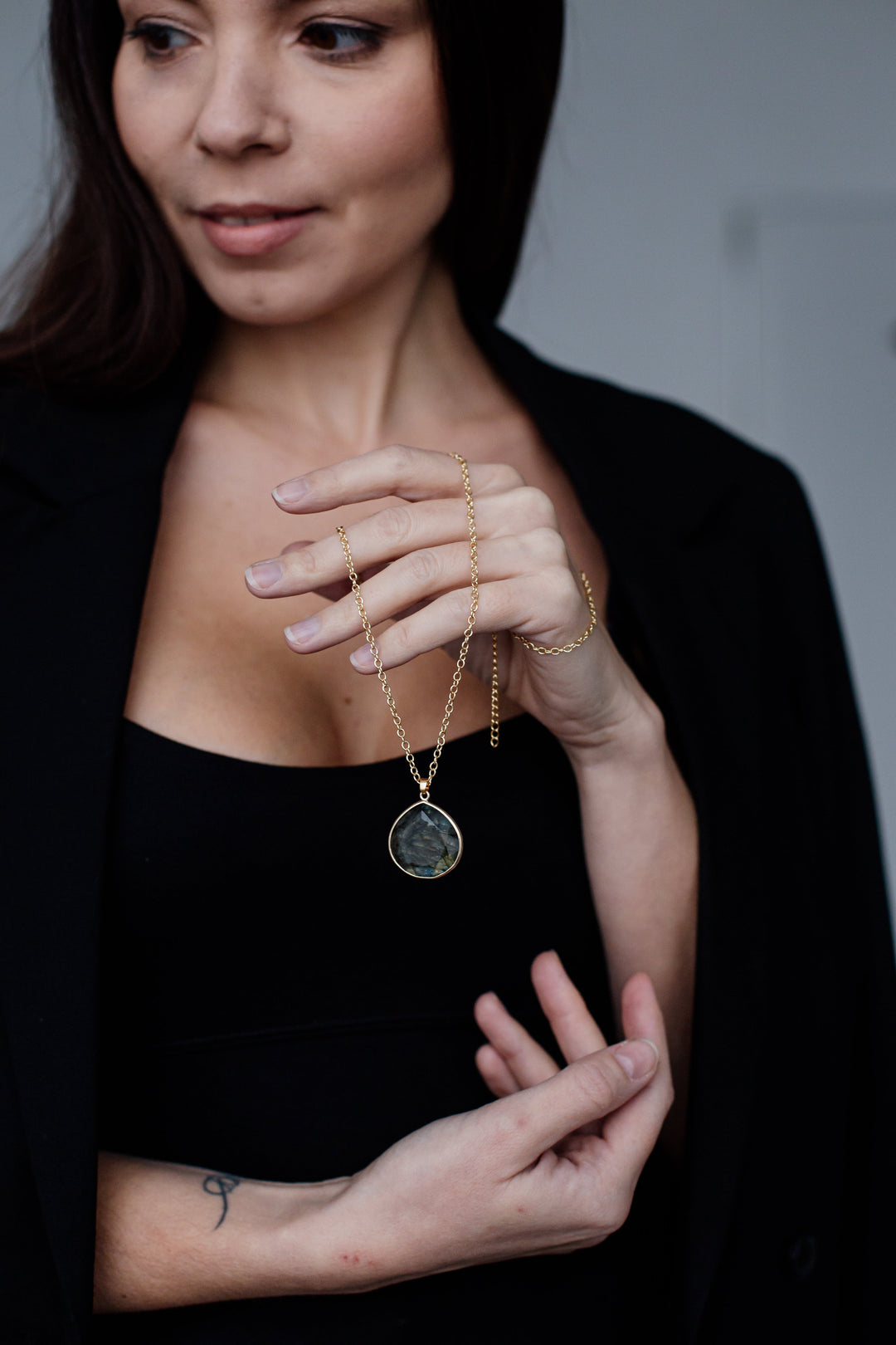 Frau mit schwarzem Blazer hält goldene Halskette mit rundem Anhänger.