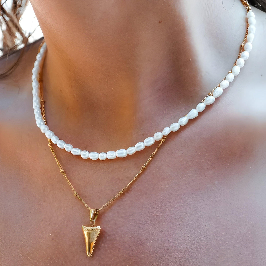 Perlenkette und goldene Haifischzahn-Halskette auf Hals, eleganter Schmuck, modisch.