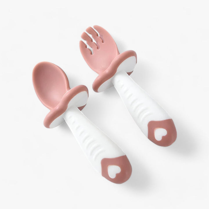 Rosa-weiße Baby-Löffel und Gabel aus Silikon mit Herzmotiv, ergonomisch geformt.