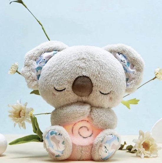 Šedobéžový plyšový koala se zavřenýma očima a růžově svítícím spirálovým bříškem mezi bílými kvítky na světle modrém pozadí. 1