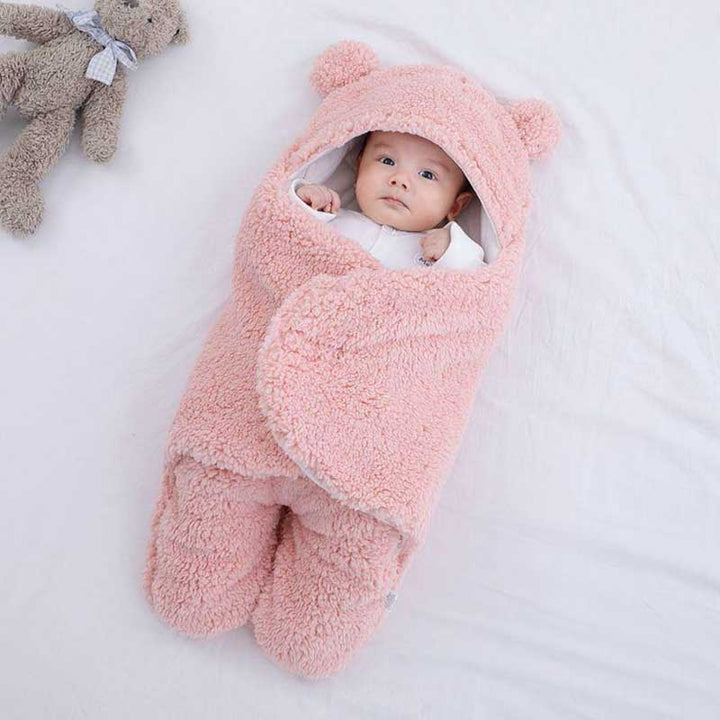 Baby in rosa, flauschiger Babydecke mit Kapuze, Bärenohren, auf weißem Hintergrund.