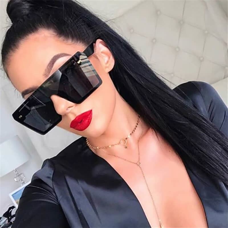 Frau mit schwarzer Sonnenbrille, rotem Lippenstift, schwarzem Outfit, modernem Stil.