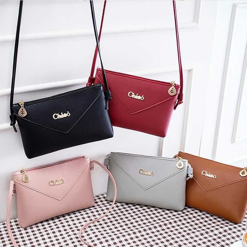 Fünf elegante Damenhandtaschen in Schwarz, Rot, Rosa, Grau und Braun auf kariertem Tisch.