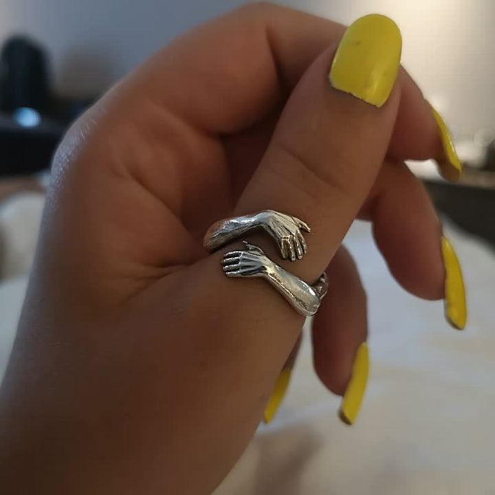 Silberner Armreif-Ring mit Handdesign, getragen an Hand mit gelbem Nagellack.
