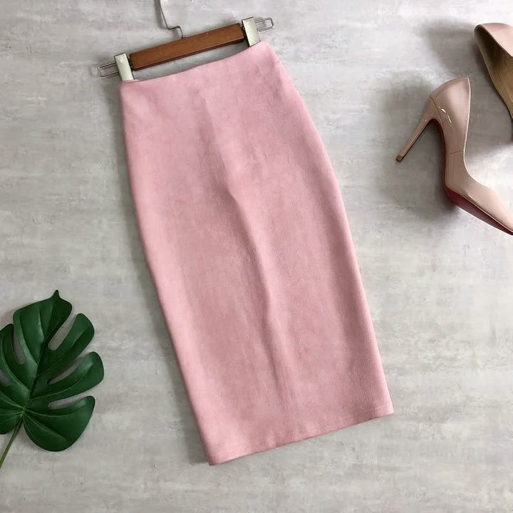 Rosa Bleistiftrock aus Baumwolle, knielang, neben beigen High Heels und grünes Blatt auf grauem Boden.
