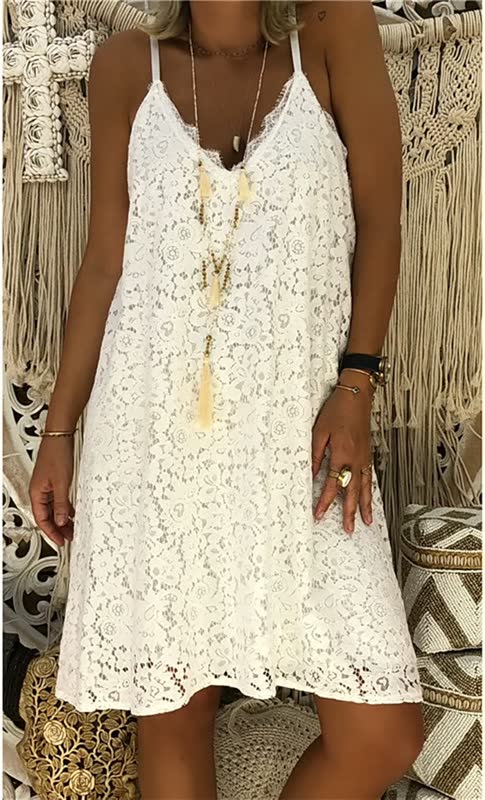 Frau in weißem Spitzenkleid, Boho-Stil, mit Schmuck, vor Makramee-Hintergrund.