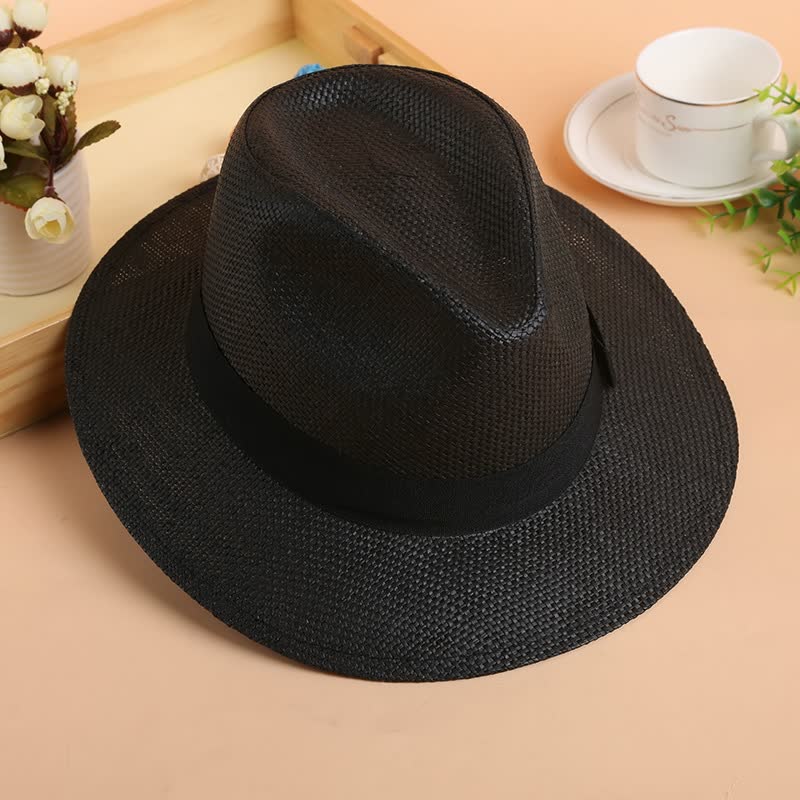 Schwarzer Fedora-Hut aus Stroh auf Tisch, stilvoller Sommerhut, Herrenmode-Accessoire.