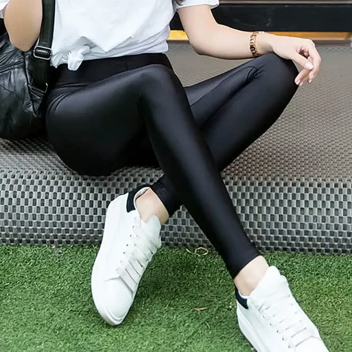 Frau in schwarzer Lederleggings und weißen Sneakers auf Teppich sitzend, modisch, bequem.