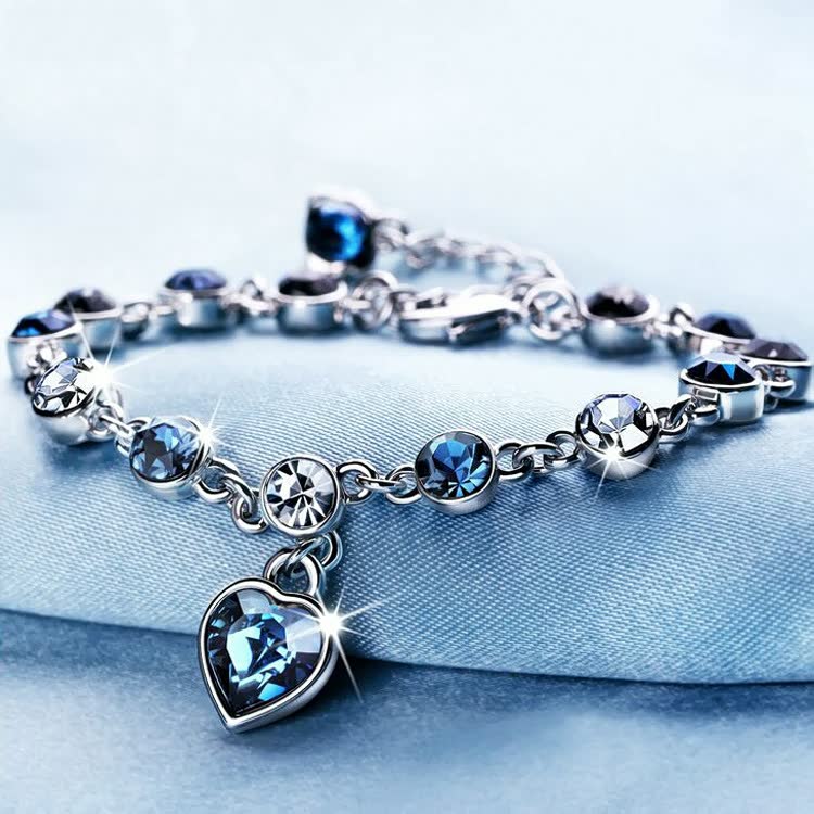 Silberarmband mit blauen Kristallen und Herzanhänger, funkelnd, elegantes Schmuckdesign.