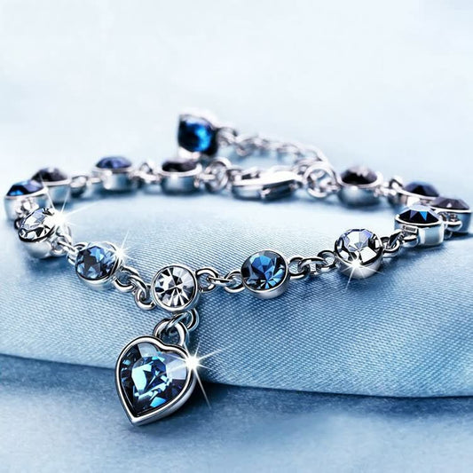 Silberarmband mit blauen Kristallen und Herzanhänger, funkelnd, elegantes Schmuckdesign.