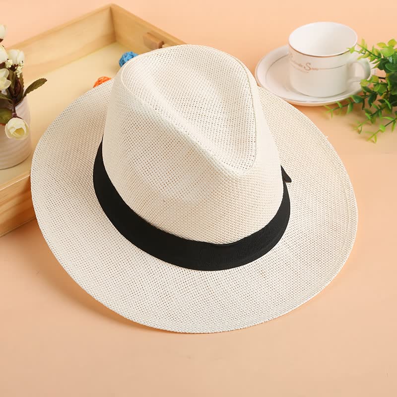 Weißer Panama-Hut aus Stroh mit schwarzem Band auf Holztisch, Sommermode-Accessoire.